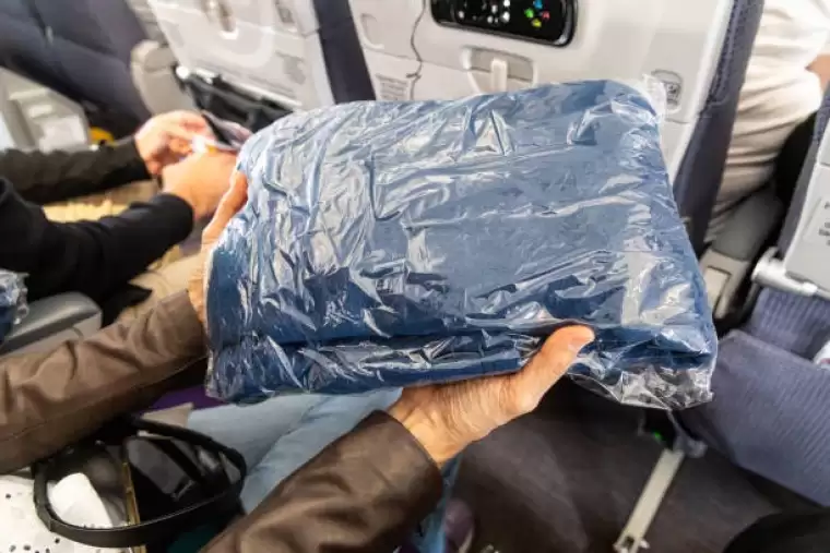passenger holding sanitized and sealed wool blanket in plastic bag provided to passengers to keep warm and comfortable during flight - battaniye stok fotoğraflar ve resimler